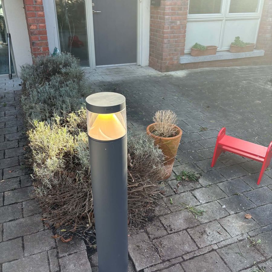 A new dark grey bollard light standing lit in the same bed beside the front door