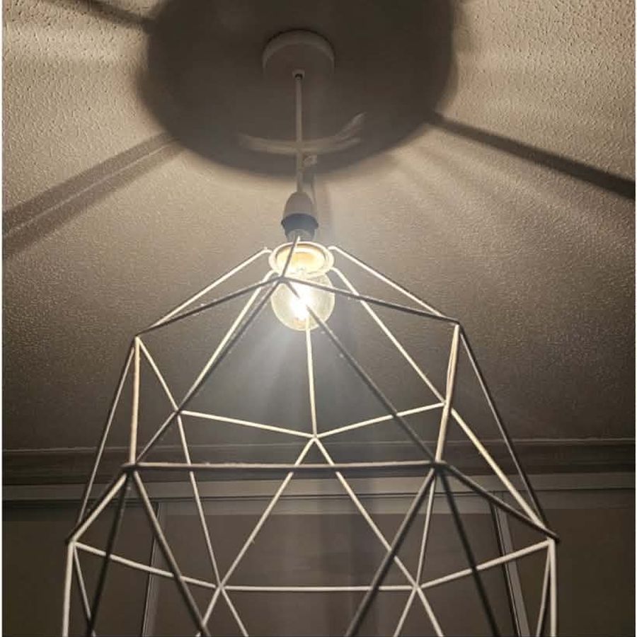A geometric wire cage pendant with a bare bulb casting harsh shadows on the ceiling